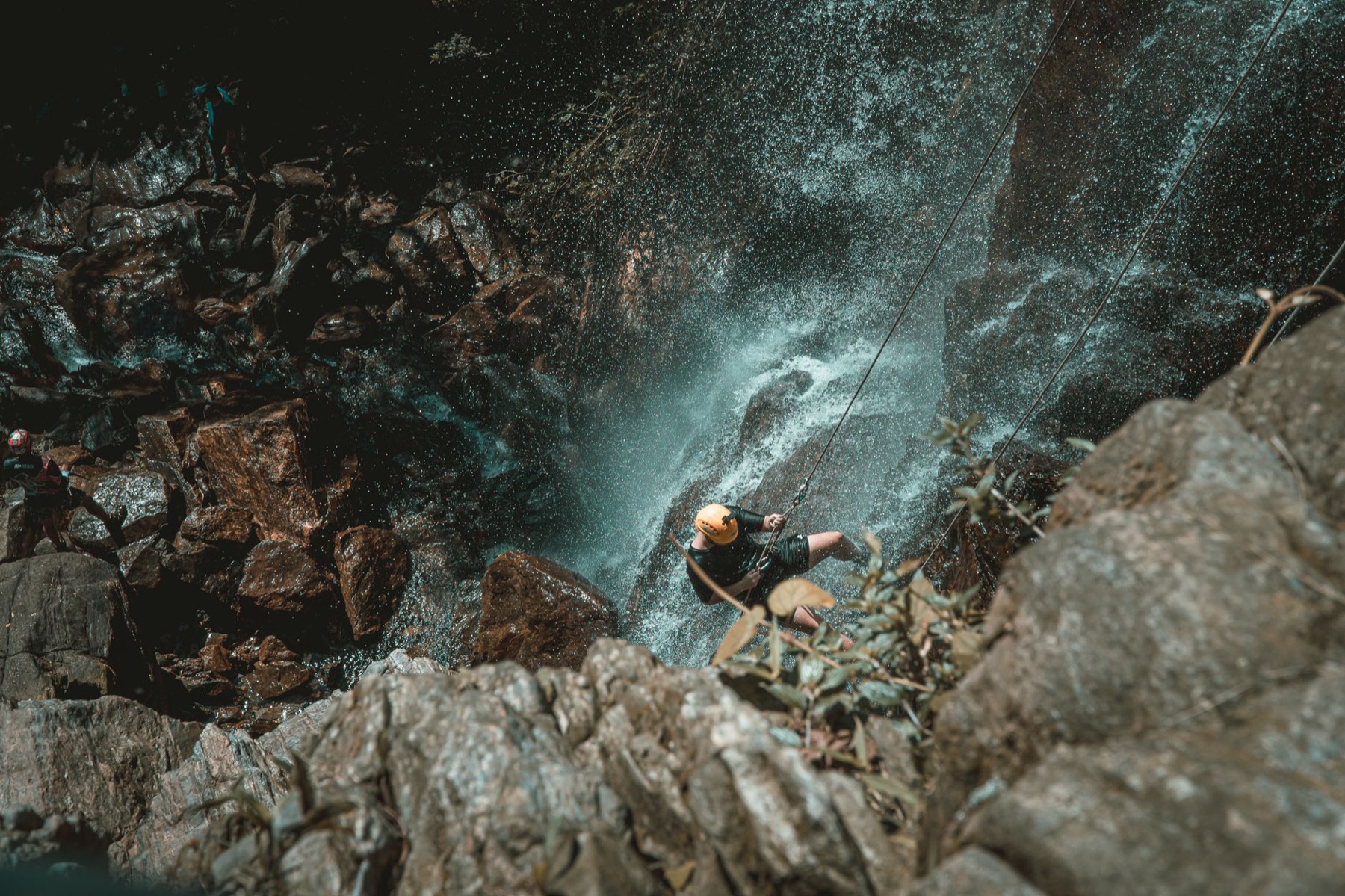 Persona en rappel descendiendo junto a una cascada entre rocas